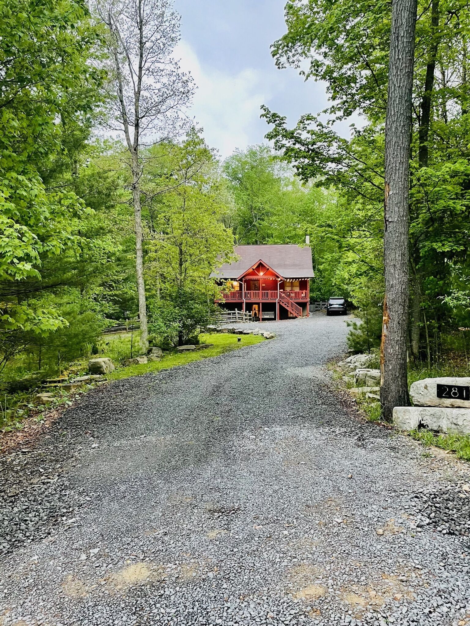 A red cabin with a gravel driveway, surrounded by trees.