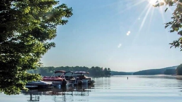 Blick auf einen See mit vor Anker liegenden Booten, einer hölzernen Bank und einer felsigen Uferlinie.