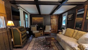 A cozy room with a wooden ceiling, a checkered sofa, a patterned rug, and a wooden cabinet. - Private, Cozy Cottage in the woods (Indian Lake)