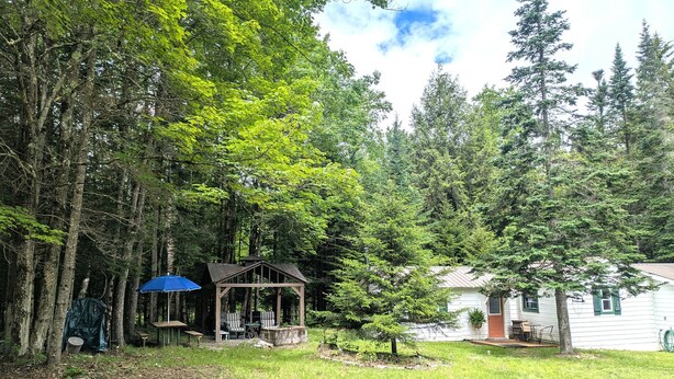 A cabin with a porch, a covered seating area, and a small shed. - Private, Cozy Cottage in the woods (Indian Lake)