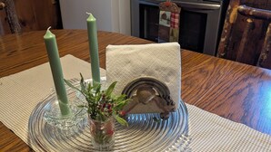 A wooden dining table with a clear glass candle holder, a white napkin, and a decorative metal piece. - Private, Cozy Cottage in the woods (Indian Lake)