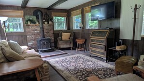 A cozy living room with a fireplace, comfortable seating, a television, and a wooden dresser. - Private, Cozy Cottage in the woods (Indian Lake)