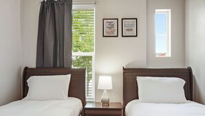 Ein Hotelzimmer mit zwei Betten, einem Nachttisch mit Lampe, einem Fenster mit Jalousien und zwei gerahmten Bildern an der Wand.
