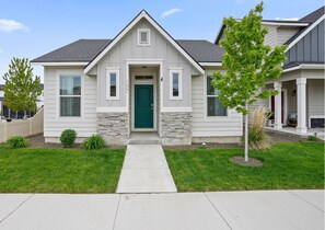 A two-story house with a green door, stone accents, and a small front yard with a tree and shrubs.