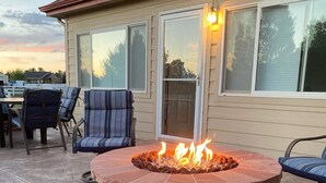 Une terrasse avec un foyer en briques, des meubles d’extérieur et une maison dotée de grandes fenêtres.