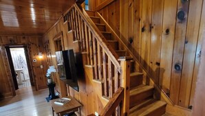 Un intérieur en bois avec un escalier, un téléviseur à écran plat fixé au mur et une table en bois.