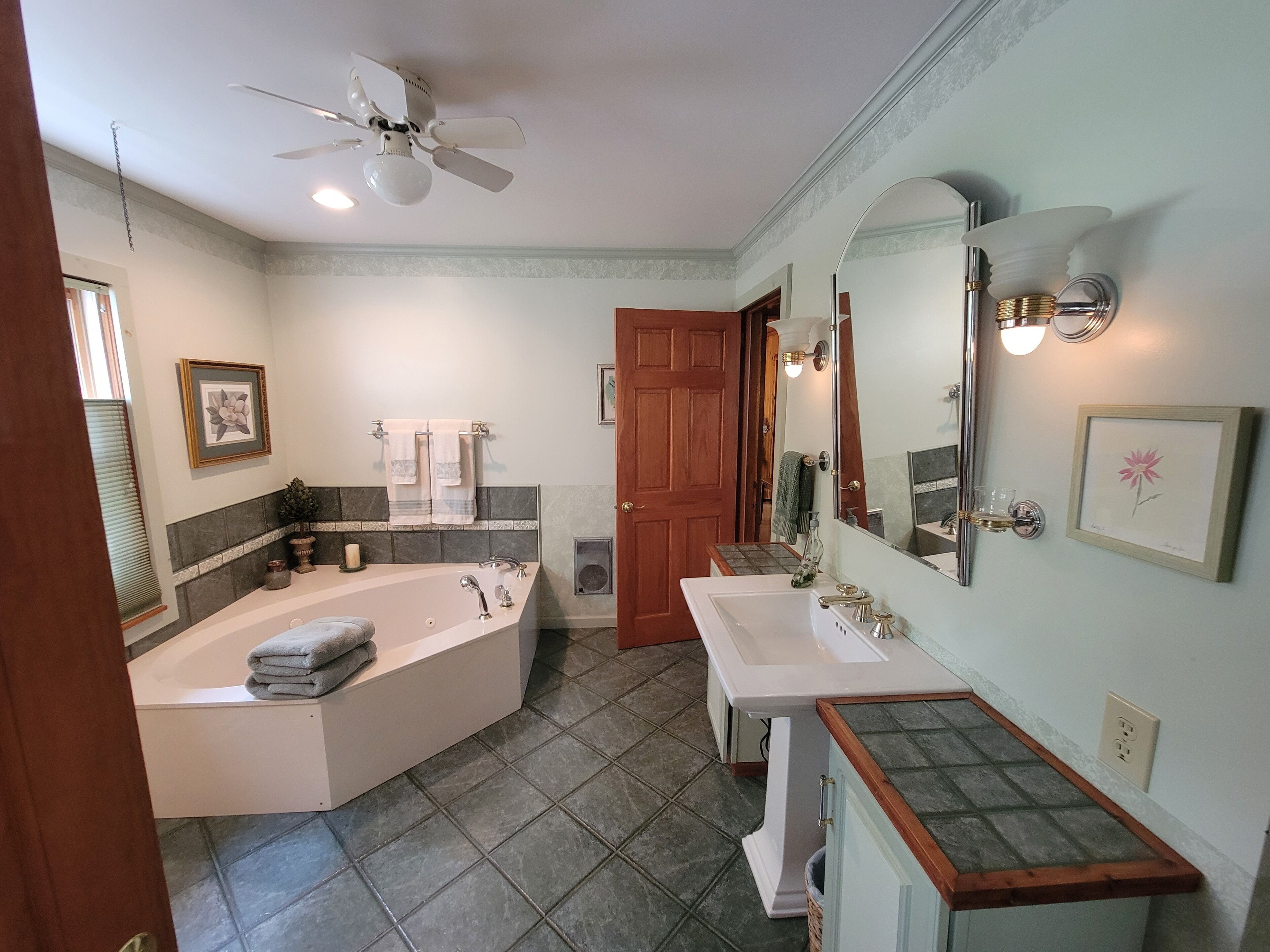 Une salle de bain avec une baignoire sur pieds, deux lavabos, un meuble-lavabo, un ventilateur de plafond et un grand miroir.