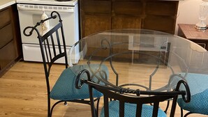 Une cuisine avec des meubles de rangement en bois, un fourneau blanc, un four à micro-ondes et une table en verre avec des chaises.