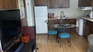 Un espace de vie compact comprenant un coin cuisine, un coin repas avec deux chaises, un téléviseur à écran plat et un réfrigérateur.