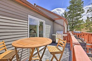 Eine Holzterrasse mit Tisch, Stühlen, einem Grill und einer Glasschiebetür, die zu einer überdachten Patio führt.