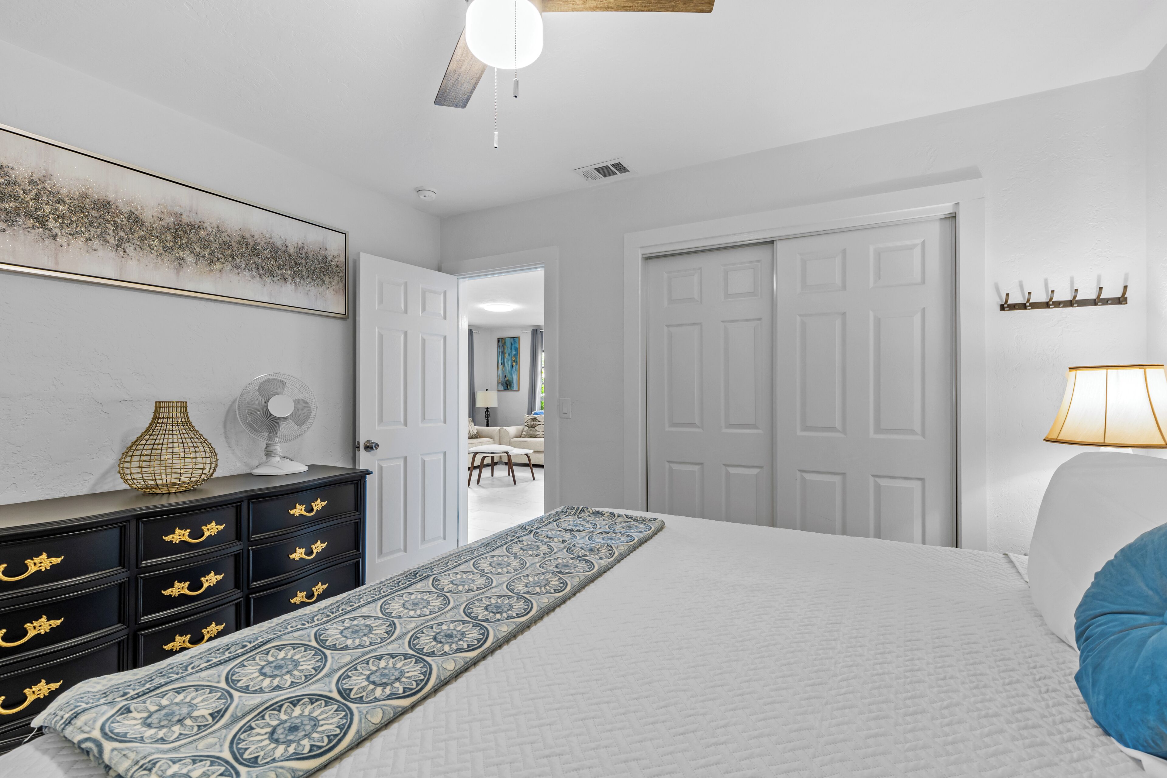 Un dormitorio con cama, cómoda, ventilador y puerta que da a otra habitación.