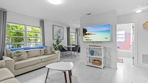A modern living room with a sofa, a coffee table, and a TV displaying a beach scene.