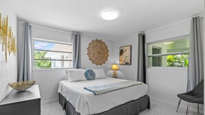 A modern bedroom with a large bed, a bedside table, a lamp, and a decorative wall piece.