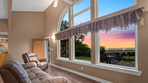 A spacious living room with a large leather sofa, a dining area with a table and chairs, and a view of a sunset through large windows. - Harbor View! Walk Out The Door Into Downtown Lex! (Lexington)