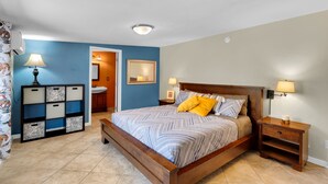 A bedroom with a wooden bed, bedside tables, a nightstand, a wall-mounted lamp, and a built-in storage unit.