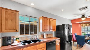 A kitchen with wooden cabinets, a black refrigerator, a coffee maker, and a window with blinds.