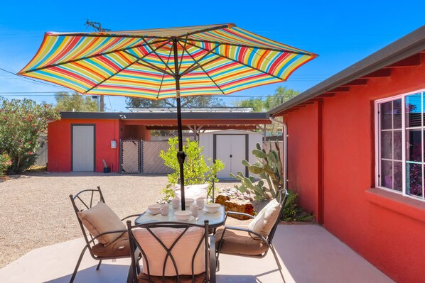 Un patio con una mesa, sillas y un colorido paraguas a rayas.