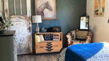 A rustic room with a bed, a dresser, a mirror, and a wall-mounted painting.