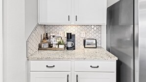 A kitchen with white cabinets, a stainless steel refrigerator, and a countertop with a coffee maker, toaster, and decorative items. - Modern & Cozy ☀ Close to Beach ☀ 4 Bedrooms ☀ 2 Full Baths (Foley)