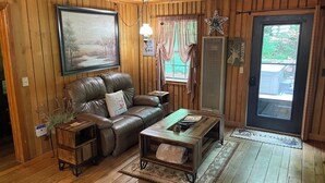 Interior acollidor d'una cabana amb un sofà de pell, una taula de centre de fusta i un ventilador de sostre.