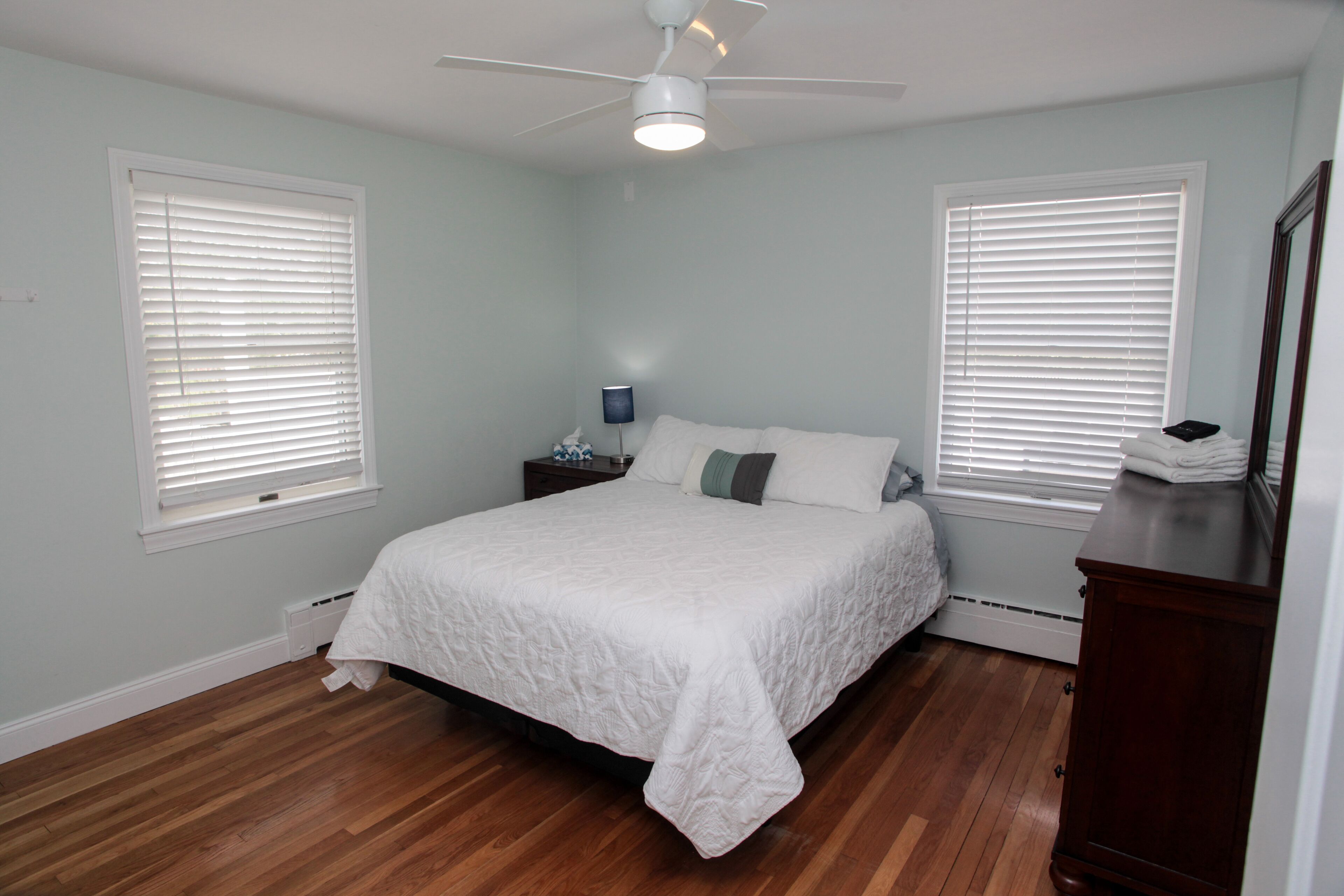 Un dormitorio con cama, mesita de noche, lámpara y ventilador de techo.