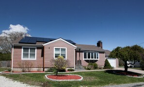 A two-story house with a solar panel roof, a front porch, and a well-maintained lawn. - Beach house walking distance to Second Beach (Middletown)