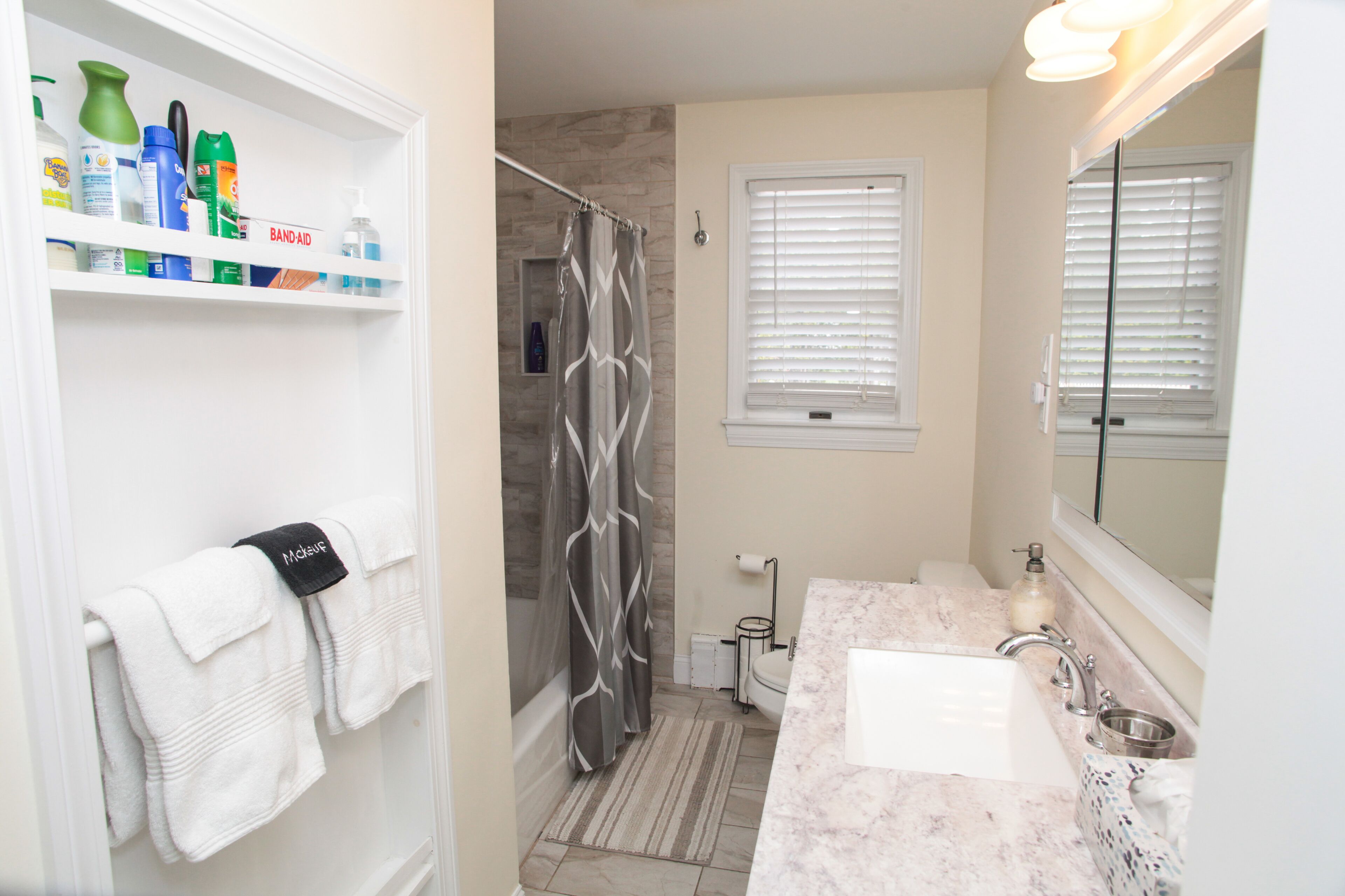 A bathroom with a shower, a sink, a mirror, and shelves with toiletries.