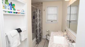 A bathroom with a shower, a sink, a mirror, and shelves with toiletries.