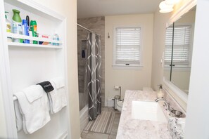 A bathroom with a shower, a sink, a mirror, and shelves with toiletries. - Beach house walking distance to Second Beach (Middletown)