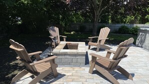 Un'area salotto esterna con poltrone in stile Adirondack e un braciere in pietra.