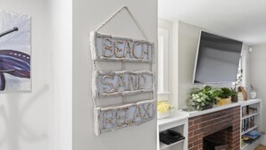 Een woonkamer met een witte muur, een open haard, een wandgemonteerde televisie en een plank met planten en boeken.