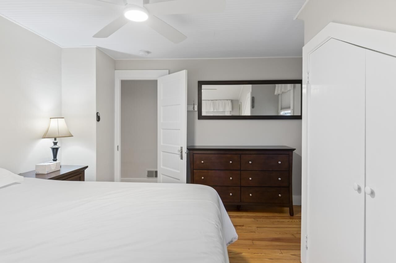 Un dormitorio con una cama, un aparador, un espejo y un ventilador de techo.