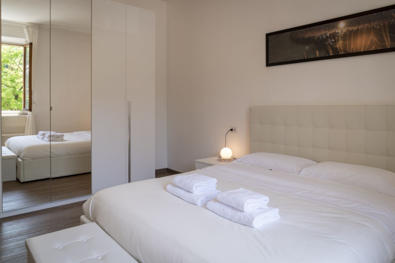Hotelkamer met een groot bed, nachtkastje met lamp, kledingkast en uitzicht op groen.