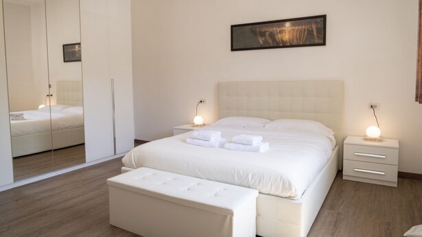 Ein modernes Schlafzimmer mit einem großen Bett, Nachttischen, einer Bank, einem Kleiderschrank und einem gerahmten Bild an der Wand.