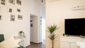 Ein modernes Wohnzimmer mit einem grünen Sofa, einem Flachbildfernseher, einer Topfpflanze und einem Flur, der in einen anderen Raum führt.