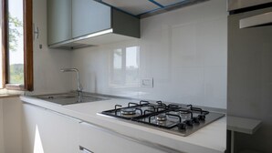 Eine moderne Küche mit weißen Schränken, einem Edelstahl-Gaskochfeld und einem Fenster, das für natürliches Licht sorgt.