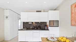 A modern kitchen with white cabinetry, a stainless steel range hood, and a wooden dining table set with a plate of lemons and wine glasses. - Downtown Cannes, Modern 1-Br. Apartment (Cannes)