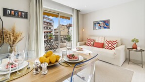 A modern living room with a dining area, featuring a sofa, a coffee table, and a view of the cityscape through large windows. - Downtown Cannes, Modern 1-Br. Apartment (Cannes)