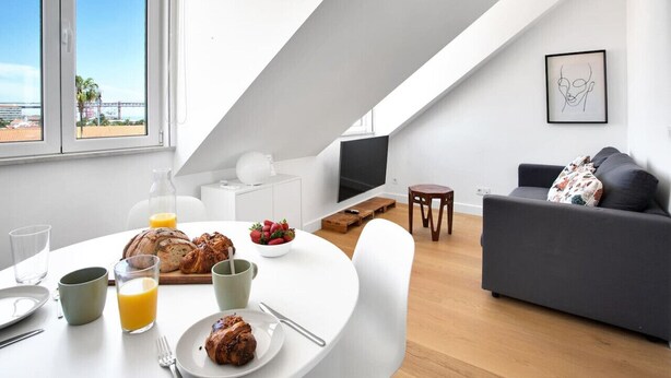 A modern living room with a white ceiling, a grey sofa, and a dining table set with breakfast items.