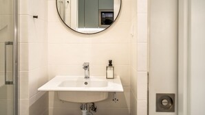Un baño con lavamanos blanco, un espejo redondo y cabina de ducha de vidrio.