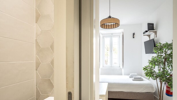 Un dormitorio moderno con cama, lámpara colgante, ventana y planta en maceta.