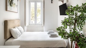 Un dormitorio con cama, ventana, planta y televisión de pantalla plana.