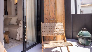 Uma varanda com uma cadeira de vime, uma porta de madeira e um vaso de cerâmica verde.