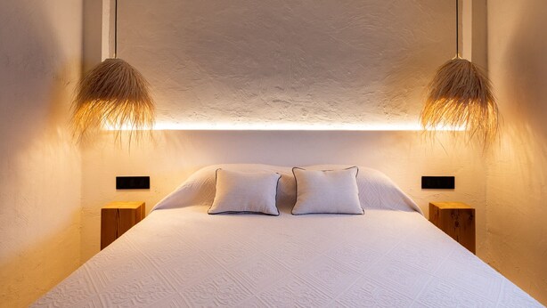 Quarto com uma cama grande, duas mesas de cabeceira e duas luminárias fixadas na parede.