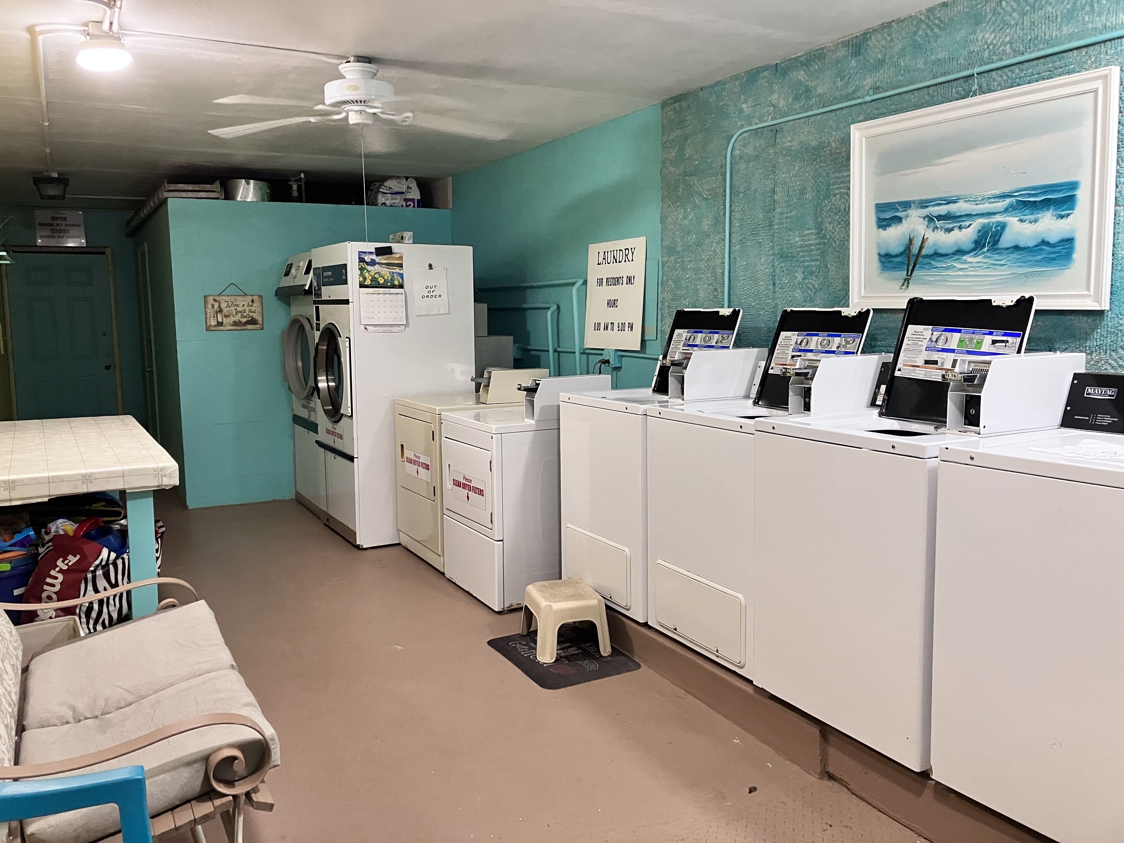 A laundry room with a ceiling fan, a washing machine, dryers, and a small stool.