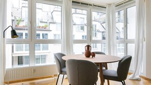 Una habitación con una mesa redonda, cuatro sillas grises, una lámpara de pie y una ventana con cortinas.