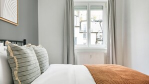 Un dormitorio con cama, ventana con cortinas y radiador.