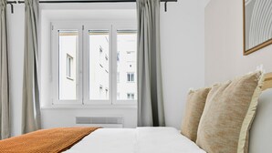Una habitación de hotel con una cama, un ventanal con cortinas y vistas a edificios.