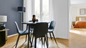 Una habitación moderna con comedor, cama y vistas a árboles por la ventana.