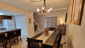 A spacious living area with a dining table, chairs, a chandelier, and a sofa.